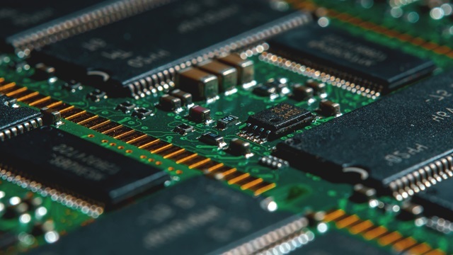 Close-up of an electronic circuit board with integrated circuits, chips, and conductive tracks, highlighting detailed components and green PCB structure.